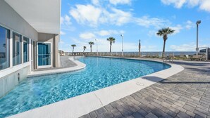 A swimming pool with clear blue water, surrounded by a paved deck and palm trees. - Beachfront Condo w/ Indoor Outdoor Pool & Grills | Gulf Shores | Sleeps 6 (Orange Beach)