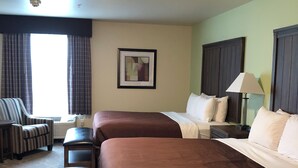 A hotel room with two beds, a desk, a chair, and a lamp.