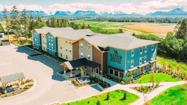 A multi-story hotel with a prominent sign, surrounded by a landscaped garden and a view of mountains.