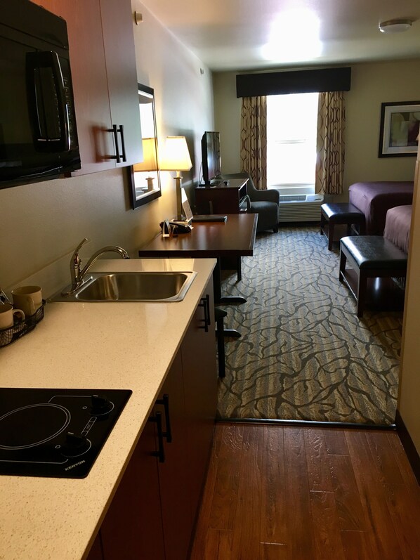 Une chambre d’hôtel compacte comprenant un coin cuisine, un espace repas, un canapé et une fenêtre avec des rideaux.