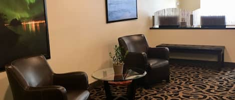 A room with two leather chairs, a glass table with a potted plant, a framed picture of the aurora borealis, and a patterned carpet.
