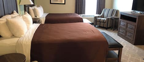 A hotel room with two beds, a desk, a chair, a TV, and an air conditioning unit.