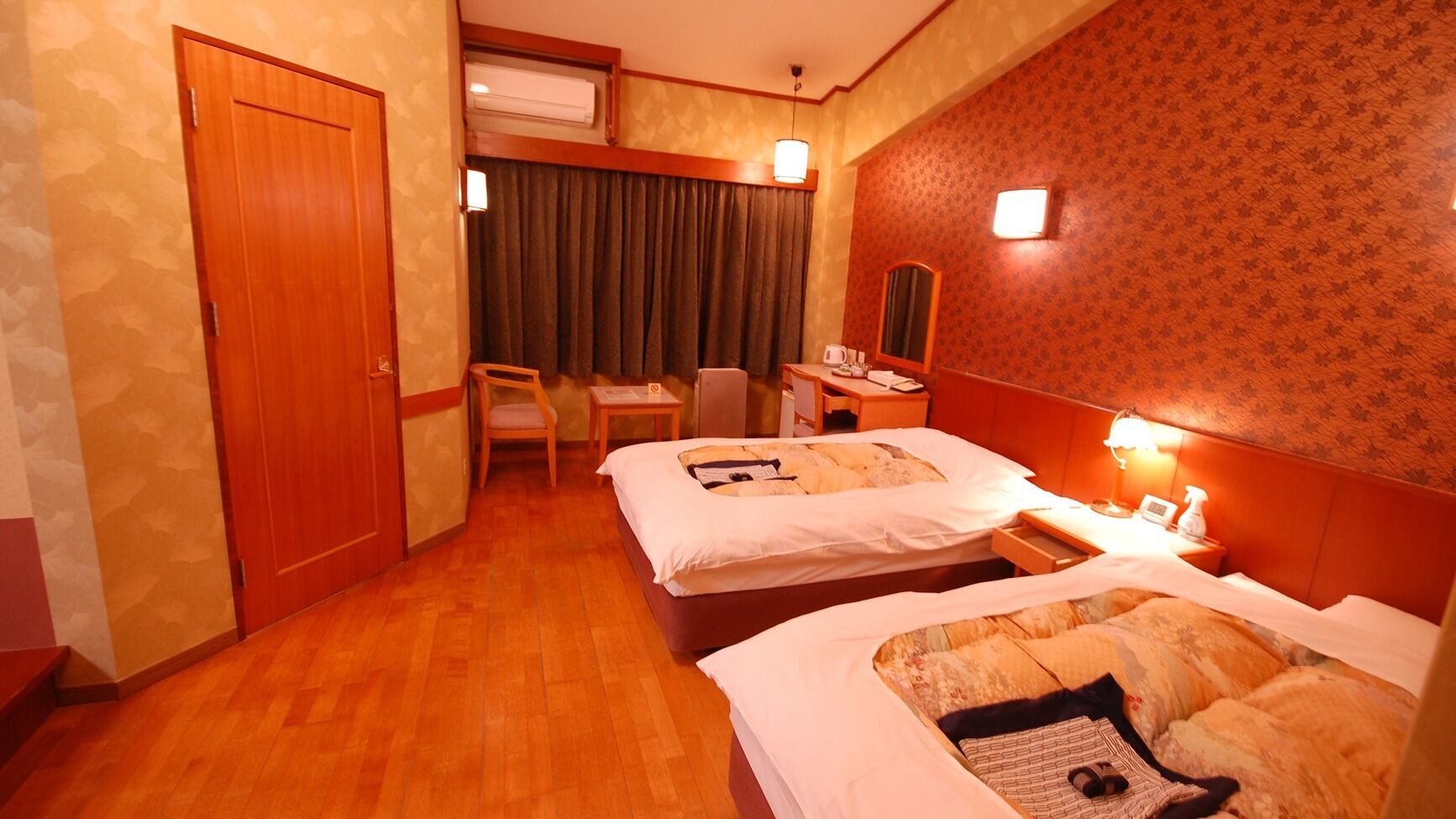 A hotel room with two beds, a desk, a chair, a mirror, and a window with curtains.