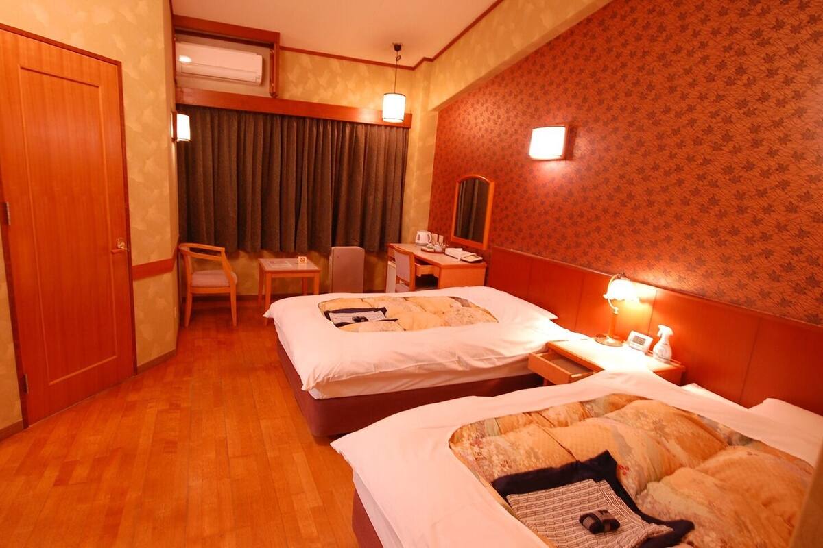 Une chambre d’hôtel avec deux lits, un bureau, une chaise, un miroir et une fenêtre avec des rideaux.