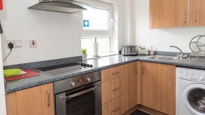Een moderne keuken met een roestvrijstalen afzuigkap, een inbouwoven, een wasmachine en houten kastjes.