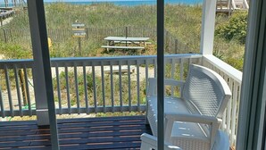 A covered outdoor area with a wooden deck, a white plastic chair, and a picnic table.