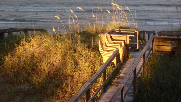 A wooden boardwalk leading to beach chairs by the ocean.