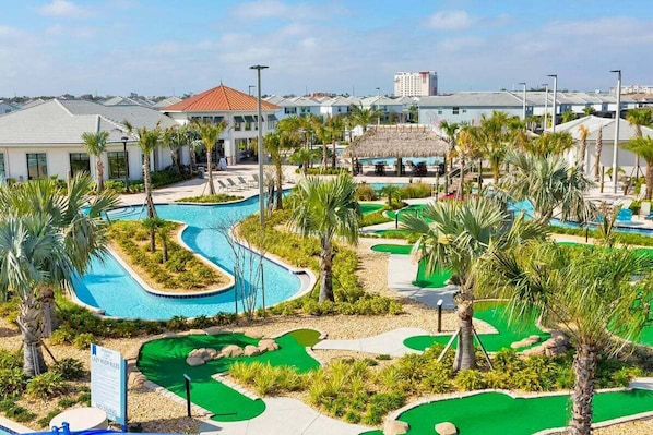 A pool area with a water slide, palm trees, and a thatched-roof structure.