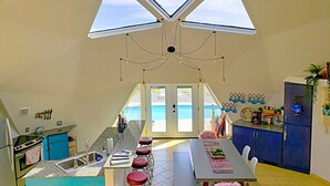 A kitchen with a central island, bar stools, a dining table, and a view of the outside.