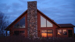 A log cabin with a stone chimney, large windows, and a view of the sunset. - Privacy and Luxury on 9 acres Overlooking Ponds & Ocean - Dog Friendly (Provincetown)