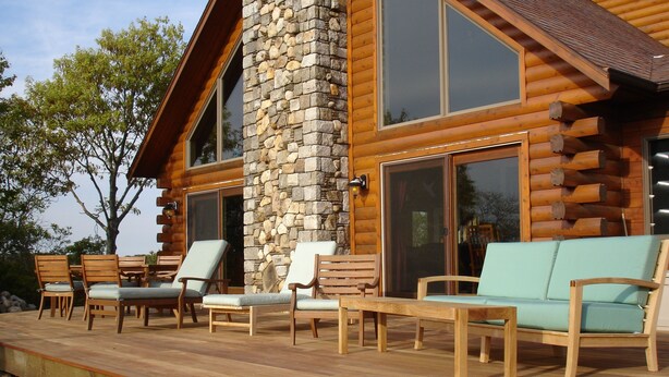 A log cabin with a wooden deck, stone pillar, and large windows. - Privacy and Luxury on 9 acres Overlooking Ponds & Ocean - Dog Friendly (Provincetown)