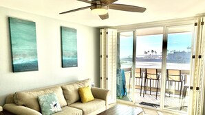 A living room with a beige sofa, a wooden coffee table, and a view of the beach through large sliding glass doors.