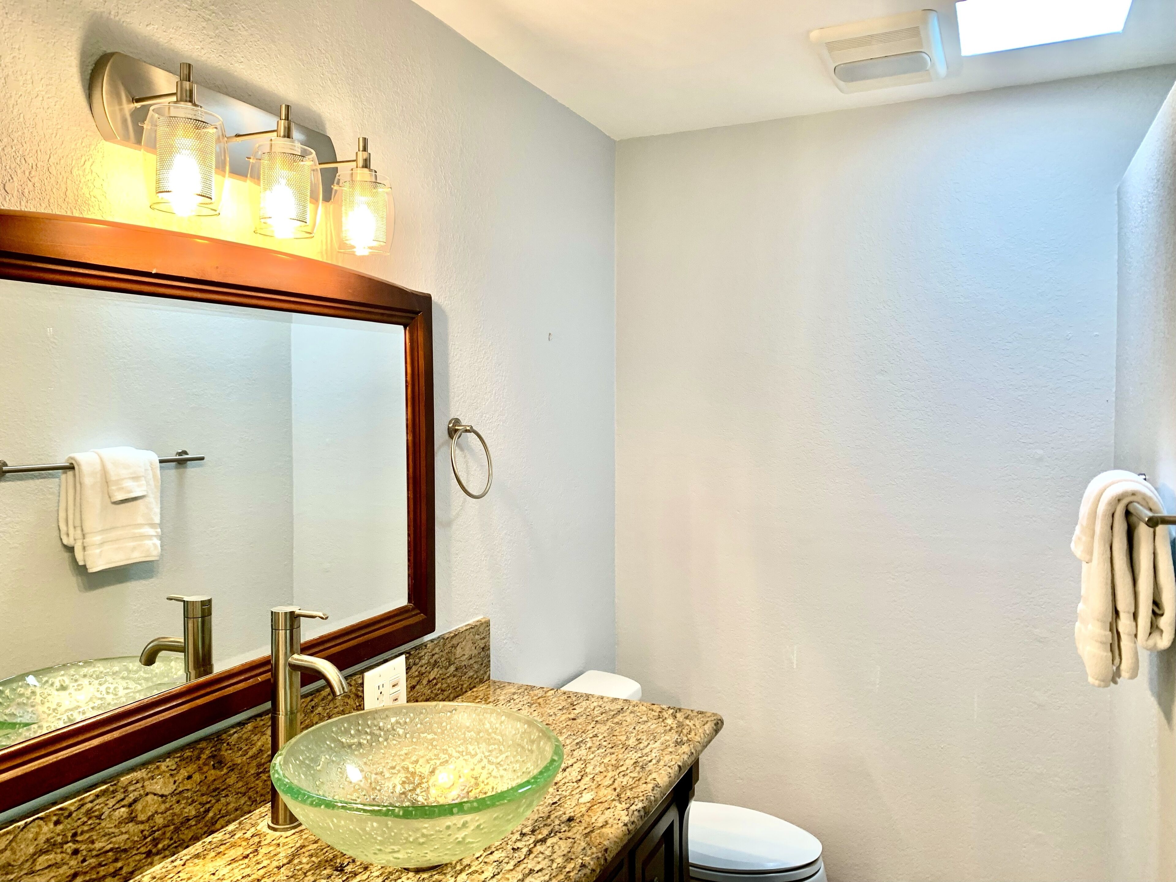 A bathroom with a large mirror, a glass bowl sink, a towel rack, and a toilet.