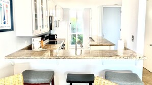 A kitchen with white cabinets, a granite countertop, and three bar stools.