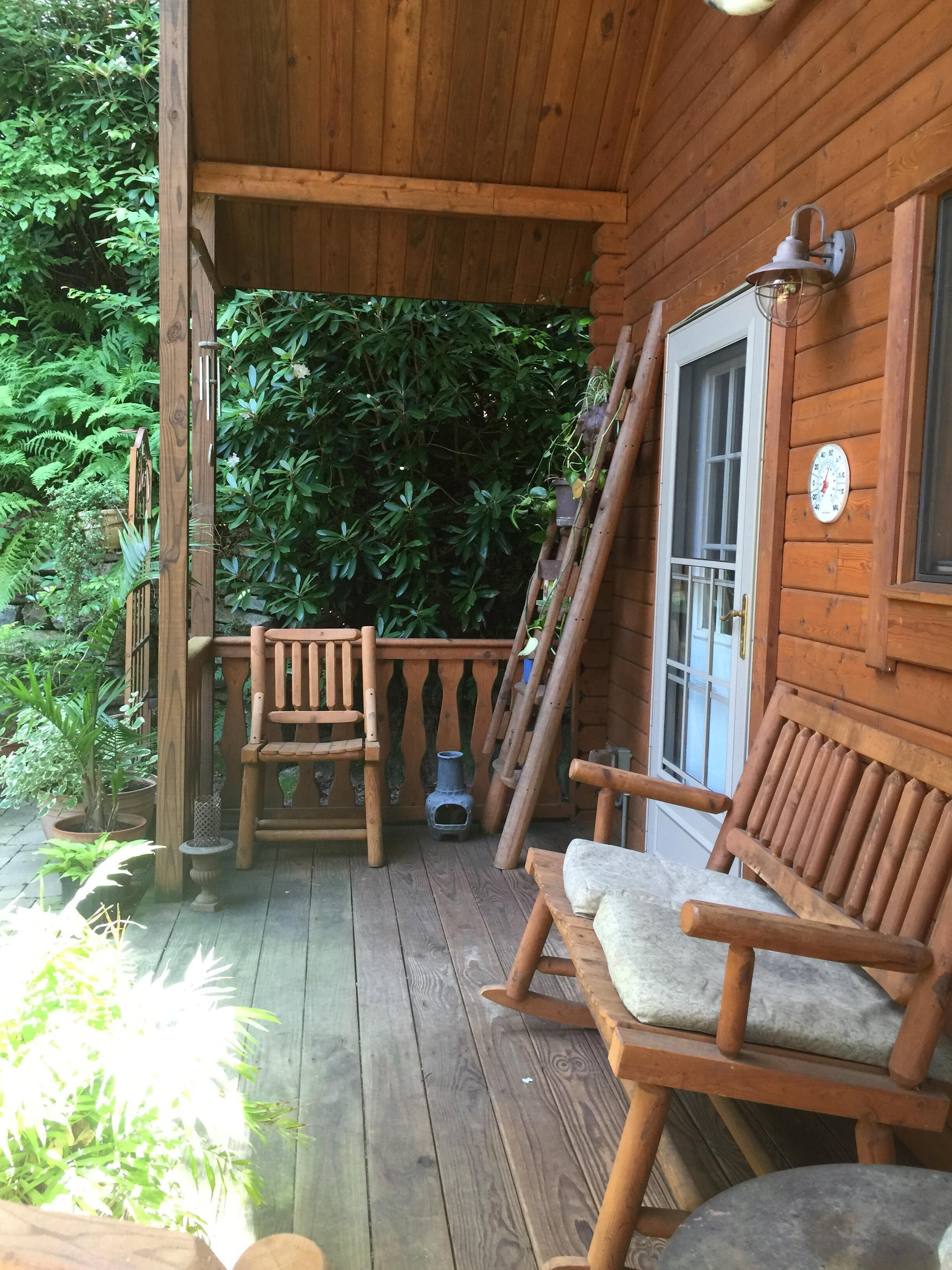 A wooden porch with two wooden chairs and a bench, a small table, and a lantern.