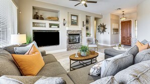 A living room with a fireplace, a ceiling fan, and a television. - Pool, Hot Tub & Golf Course View! ‘Anthem Oasis’ (Anthem)