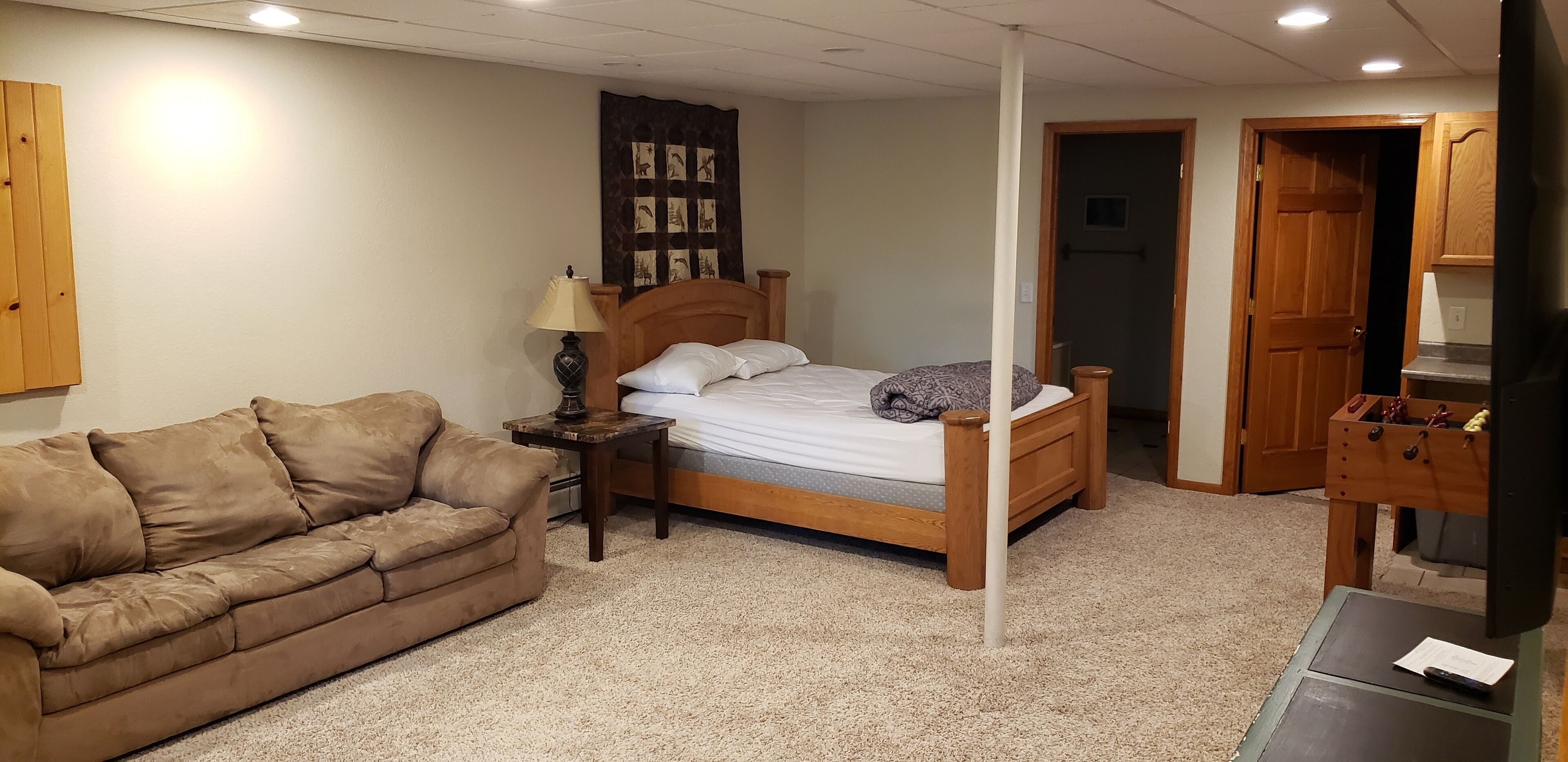 A bedroom with a wooden bed, a brown sofa, a nightstand with a lamp, and a wooden wardrobe.
