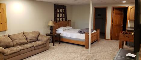 A bedroom with a wooden bed, a brown sofa, a nightstand with a lamp, and a wooden wardrobe.
