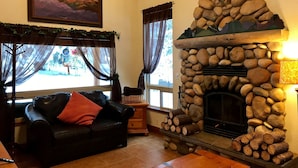 Una sala de estar acogedora con chimenea de piedra, un sofá de cuero negro con un cojín rojo, y un cuadro sobre la chimenea.