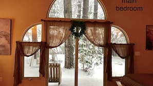 Un dormitorio principal con amplias ventanas de arco, un banco de madera en el exterior y una guirnalda en el alféizar.