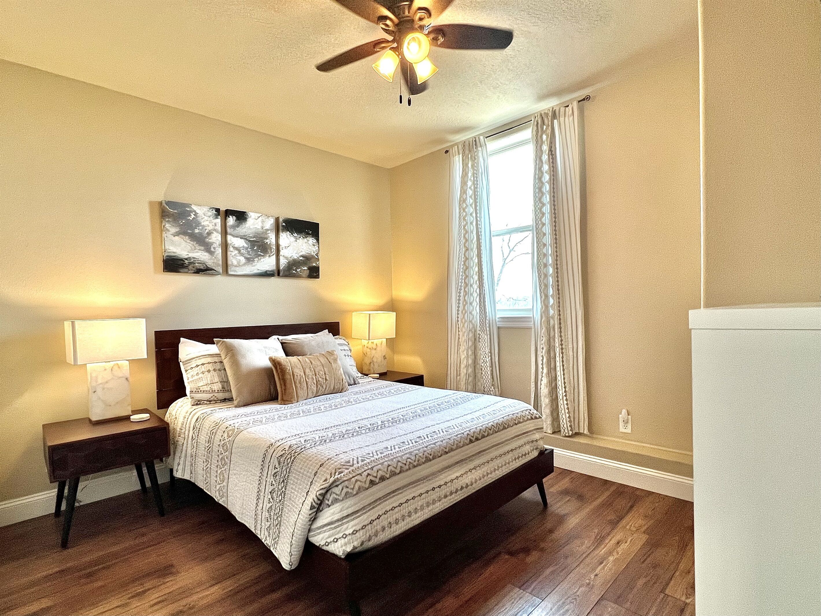 A bedroom with a bed, two bedside tables, a ceiling fan, and a window with curtains.