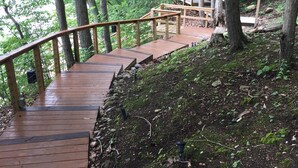 Un escalier en bois menant au sommet d’une colline boisée, avec une rampe également en bois.