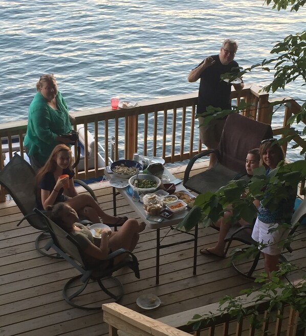 A deck with a table set for a meal, surrounded by chairs, overlooking a body of water.