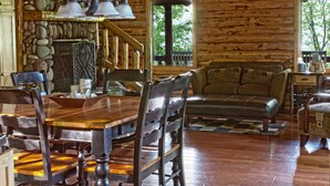 L’intérieur d’un chalet rustique, avec une table à manger en bois, des chaises, un canapé et un mur en pierre.