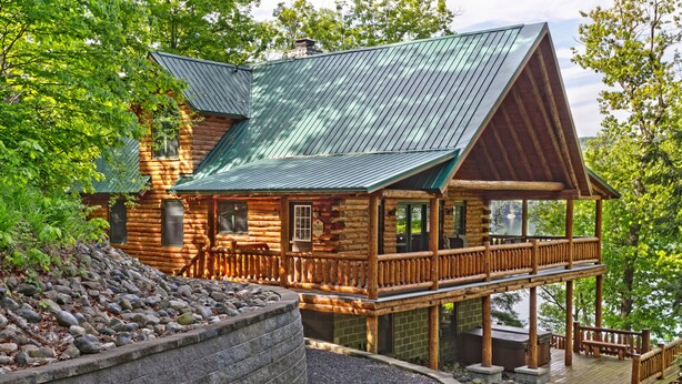 Une cabane en rondins avec un toit en métal, une terrasse et un mur de soutènement en pierre.