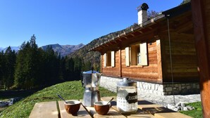 A wooden cabin with a stone foundation, a wooden table with two cups and a coffee pot, and a large jar labeled "ZUCCHEN". - CHALET BRENTA DOLOMITES (Madonna di Campiglio)