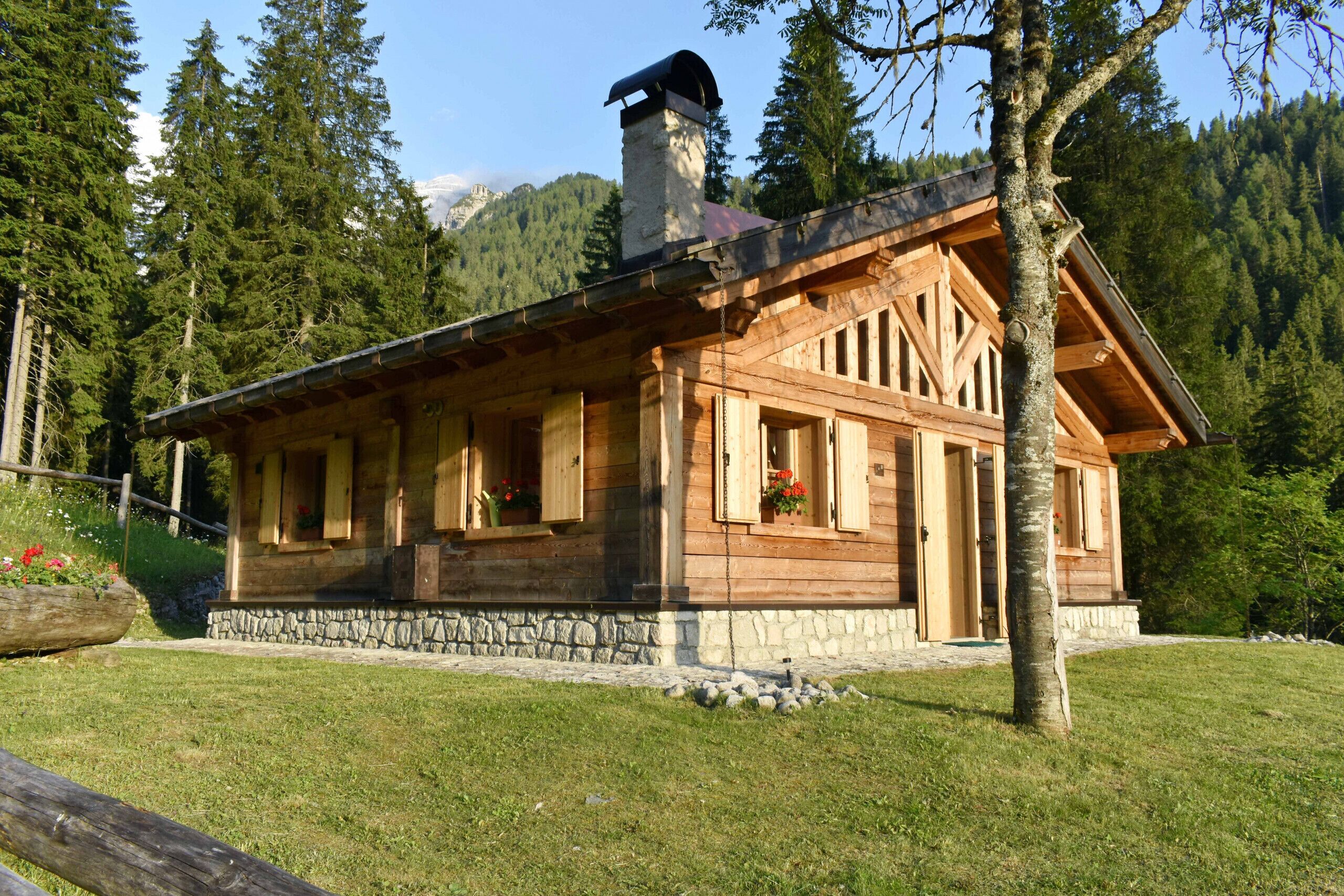 A wooden cabin with a stone foundation, large windows, and a chimney.