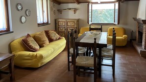 A cozy room with a wooden ceiling, a yellow sofa, a dining table with chairs, and a fireplace.