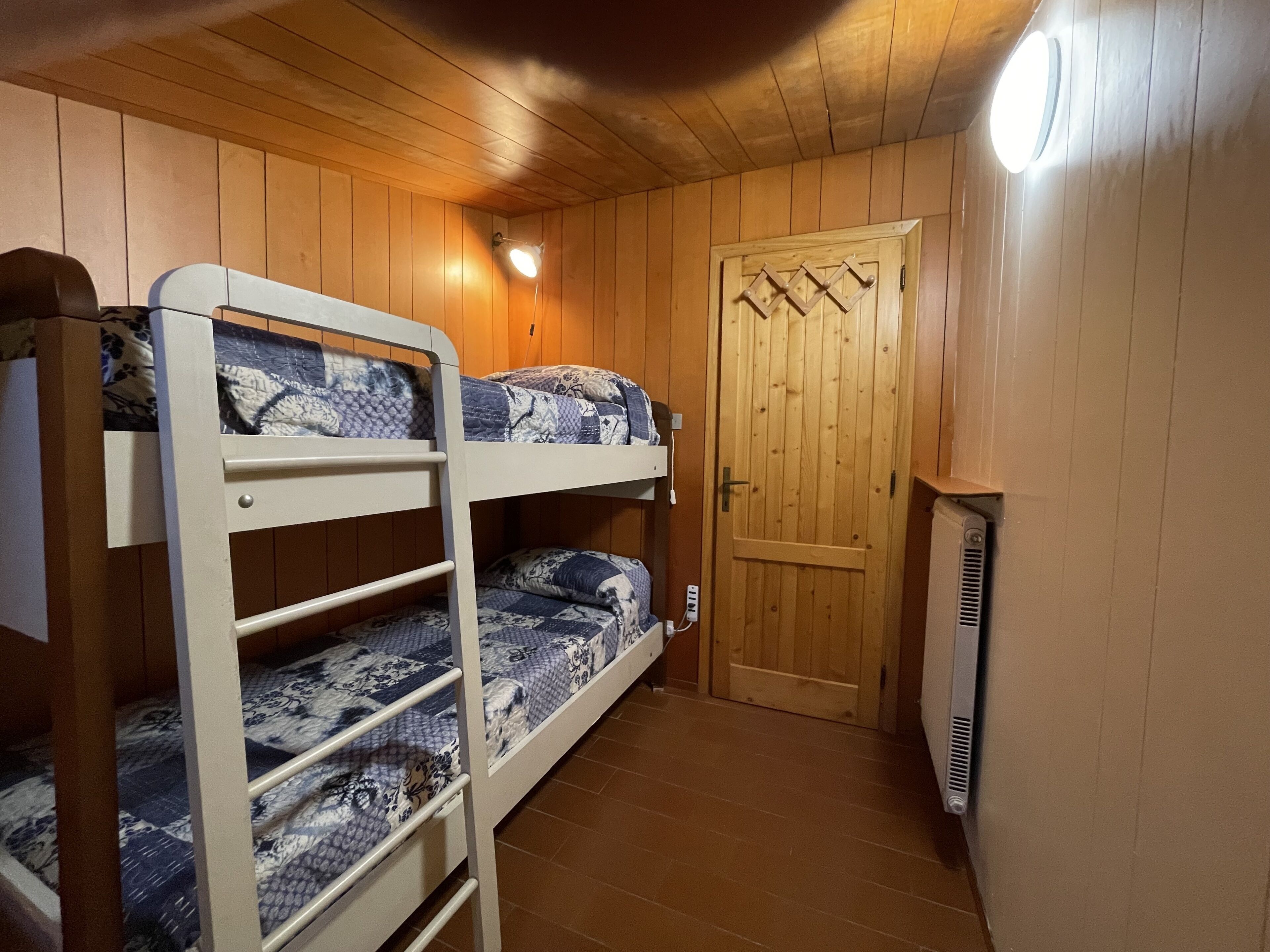 Een kamer met twee stapelbedden, een houten deur en een wandradiator.