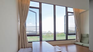 Una habitación moderna con un ventanal grande, una mesa de madera y dos zonas de estar con cojines.