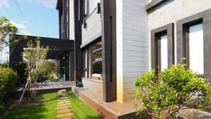 Una casa moderna con un camino empedrado que lleva a la entrada, rodeada de vegetación y un pequeño árbol.