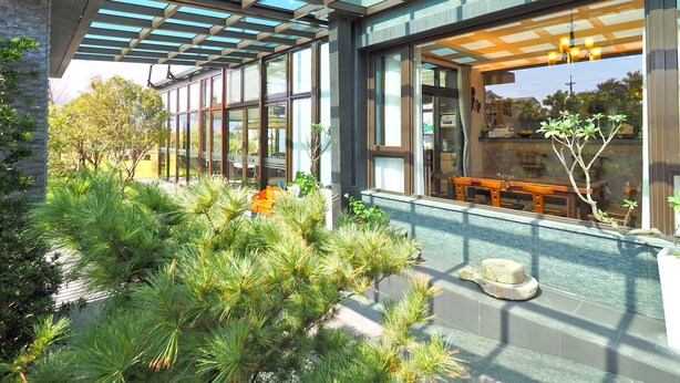 Un edificio moderno con fachada de vidrio, zona de estar al aire libre y vegetación.