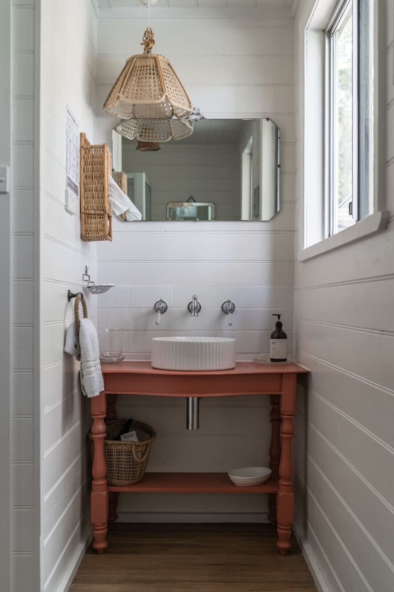 A narrow bathroom with a wooden vanity, a white sink, and a mirror above it.