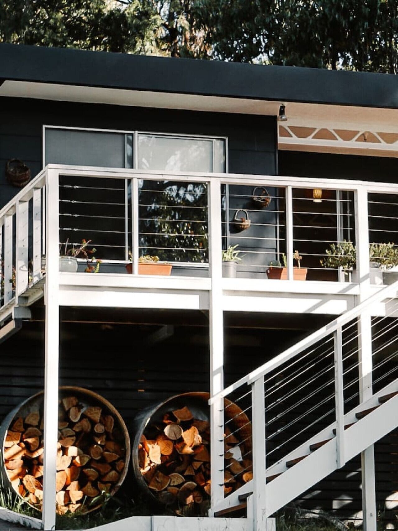 A modern house with a white exterior, a balcony with railings, and a wooden deck with firewood.