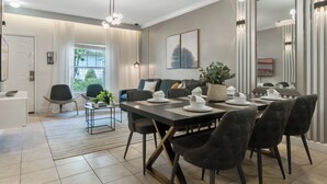 A modern dining area with a large table set for four, a sofa, and a large mirror. - 3 BD/ 2 BA/ Lucaya Village (6-107) (Kissimmee)