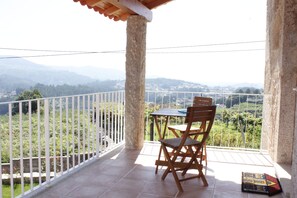 A balcony with a table and chairs, offering a view of a vineyard and distant hills. - House Nininha - T1 Azulão (Vale de Cambra)