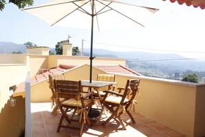 A patio with a table and chairs, an umbrella, and a view of distant hills. - House Nininha - T1 Azulão (Vale de Cambra)