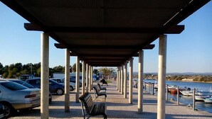Une allée couverte avec des bancs, un espace de stationnement et des bateaux amarrés au bord de l’eau.