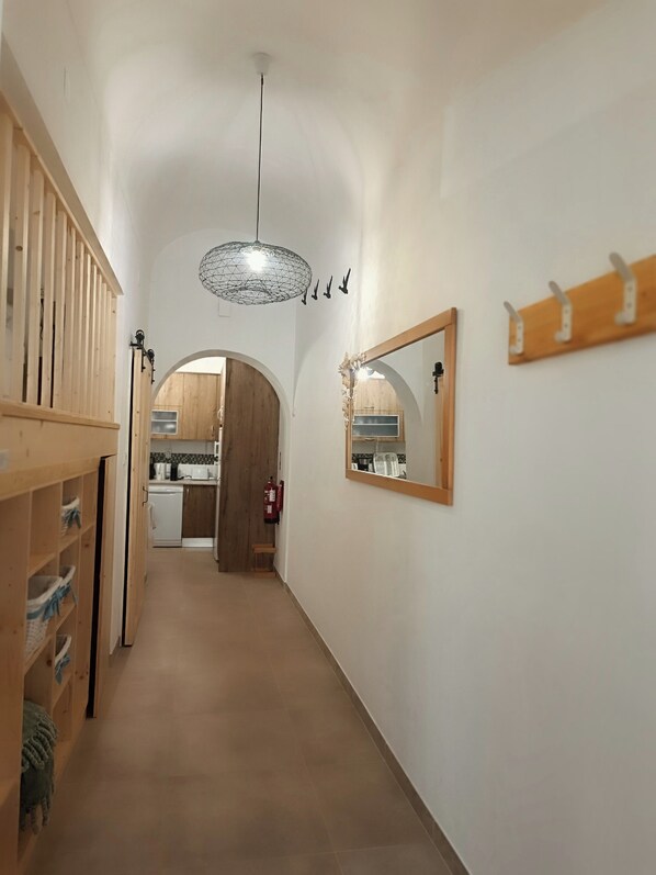 A hallway with a wooden bench, a hanging light fixture, a coat rack, and a kitchen visible through an archway. - Sea House (FUSETA)