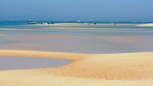 Une plage avec un ciel dégagé, une eau calme et peu de monde.