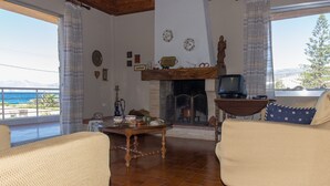 A living room with a fireplace, a television, and a view of the sea. - SUNSET BEACH HOUSE IN ALEPOCHORI (ATTIKI)