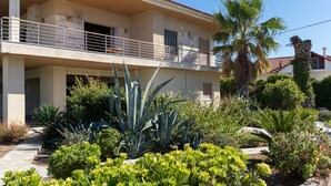 A two-story building with a balcony, surrounded by various plants and a palm tree. - SUNSET BEACH HOUSE IN ALEPOCHORI (ATTIKI)