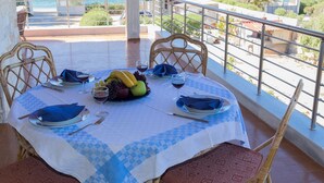 A dining table set with plates, cutlery, and fruit, overlooking a coastal view with boats. - SUNSET BEACH HOUSE IN ALEPOCHORI (ATTIKI)