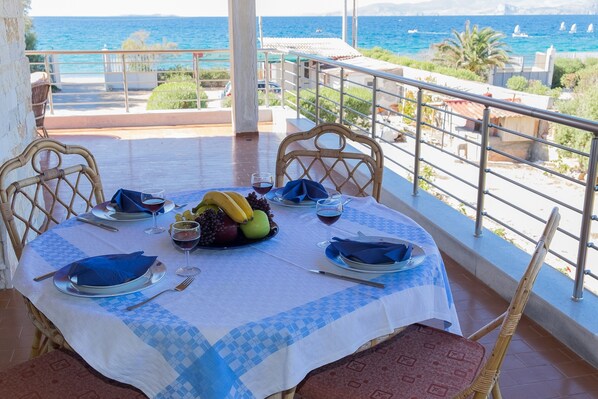 A dining table set with plates, cutlery, and fruit, overlooking a coastal view with boats.