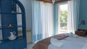 A bedroom with a bed, a blue shelving unit, a window with curtains, and a view of greenery outside. - SUNSET BEACH HOUSE IN ALEPOCHORI (ATTIKI)