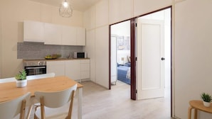 Une cuisine moderne avec des meubles blancs, un plan de travail en granit et un coin repas comprenant une table et des chaises en bois.